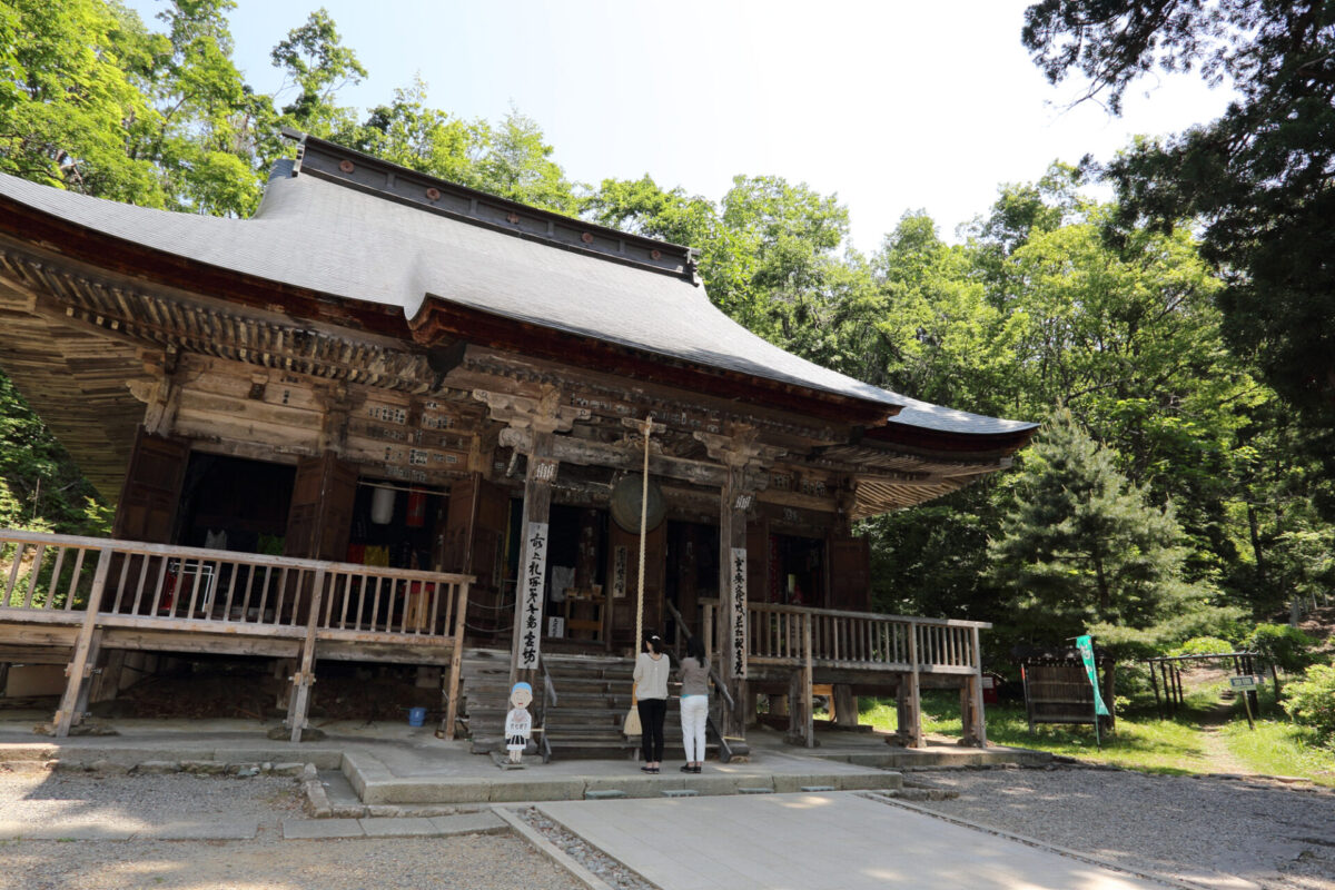 Traditional wooden Korean temple with a curved roof surrounded by green trees; two visitors at the entrance.