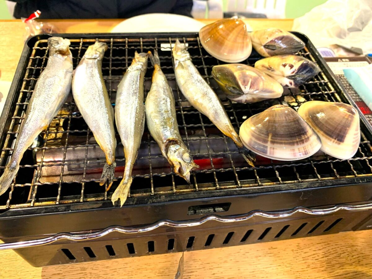 烧烤海鲜：几条完整的鱼和蛤蜊在烤架上烤制，供人享用。