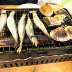 Grilled seafood on a barbecue: several whole fish and clams cooking on a wire grate grill for a meal