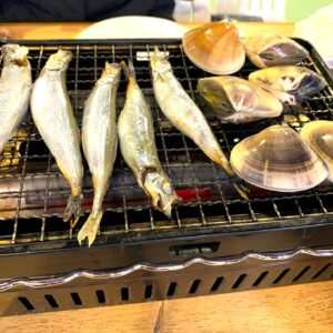 Mariscos a la parrilla: varios pescados enteros y almejas cocinándose en una parrilla de alambre para una comida