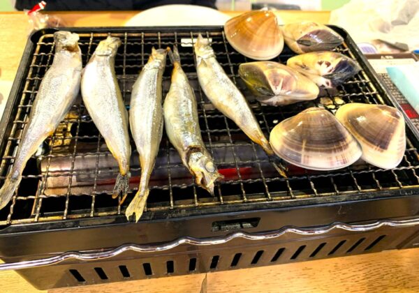 烧烤海鲜：几条完整的鱼和蛤蜊在烤架上烤制，供人享用。