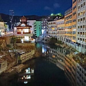 Canal nocturne d'une ville, avec un bâtiment traditionnel illuminé au centre, se reflétant sur l'eau, bordé de hauts immeubles d'appartements.