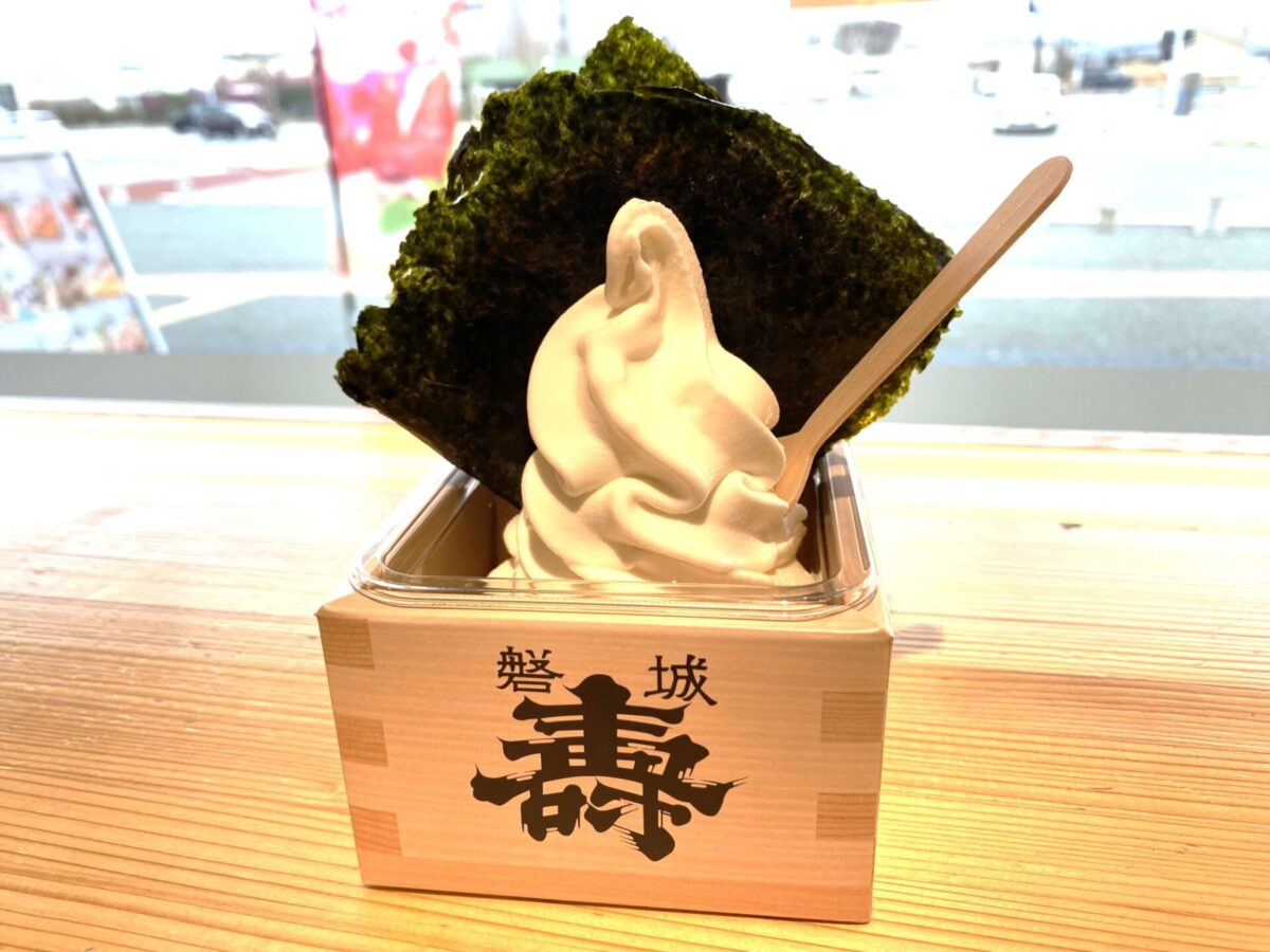 一杯香草软冰淇淋，上面放着一大片海苔，旁边木桌上放着一把木勺。.