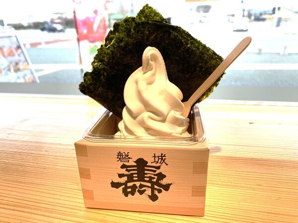 Vanilla soft-serve ice cream in a cup, topped with a large sheet of seaweed and a wooden spoon nearby on a wooden table.