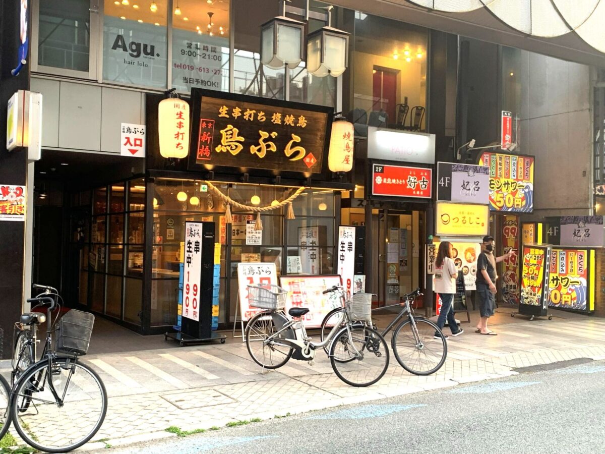 Street view of a Japanese storefront with illuminated red lanterns and bold black signboards, bicycles parked along the curb