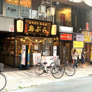 Street view of a Japanese storefront with illuminated red lanterns and bold black signboards, bicycles parked along the curb