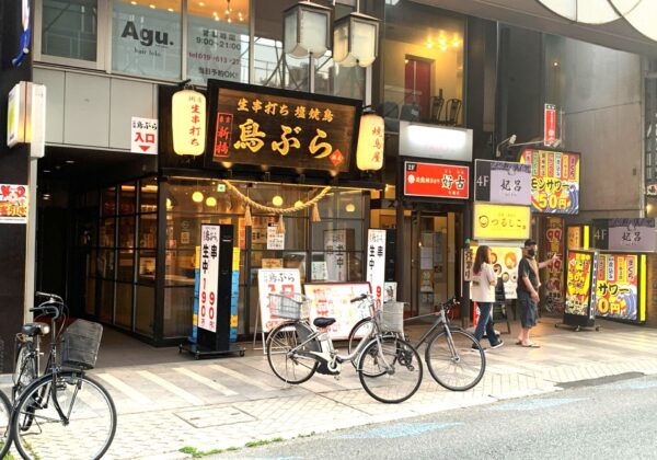Street view of a Japanese storefront with illuminated red lanterns and bold black signboards, bicycles parked along the curb