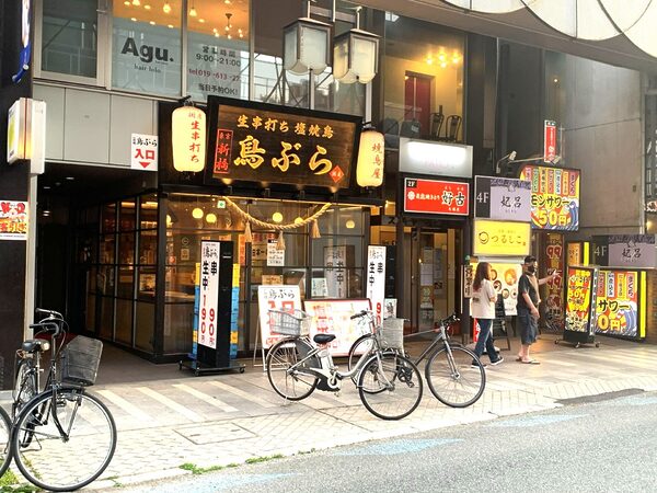 Street view of a Japanese storefront with illuminated red lanterns and bold black signboards, bicycles parked along the curb