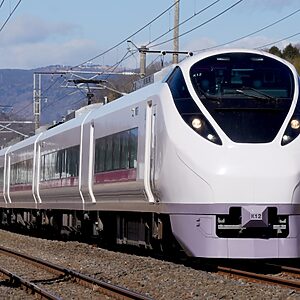 Modern white passenger train traveling on railway tracks, front-on view with overhead electric lines visible.