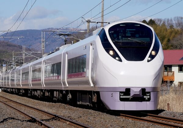 Modern white passenger train traveling on railway tracks, front-on view with overhead electric lines visible.