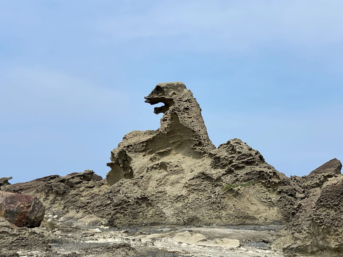 Jagged beige rock formation with a hollow arch reassembling a dragon head against a clear blue sky.