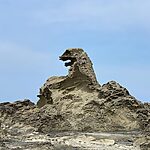 Jagged beige rock formation with a hollow arch reassembling a dragon head against a clear blue sky.