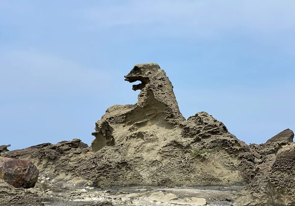 Formación rocosa irregular de color beige con un arco hueco que recuerda a la cabeza de un dragón contra un cielo azul claro.
